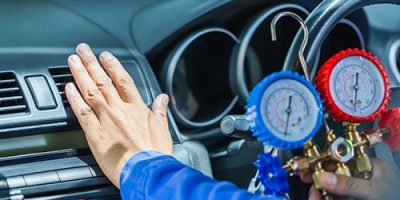Auto mechanic checking a car’s air conditioning system with diagnostic gauges under the hood.
